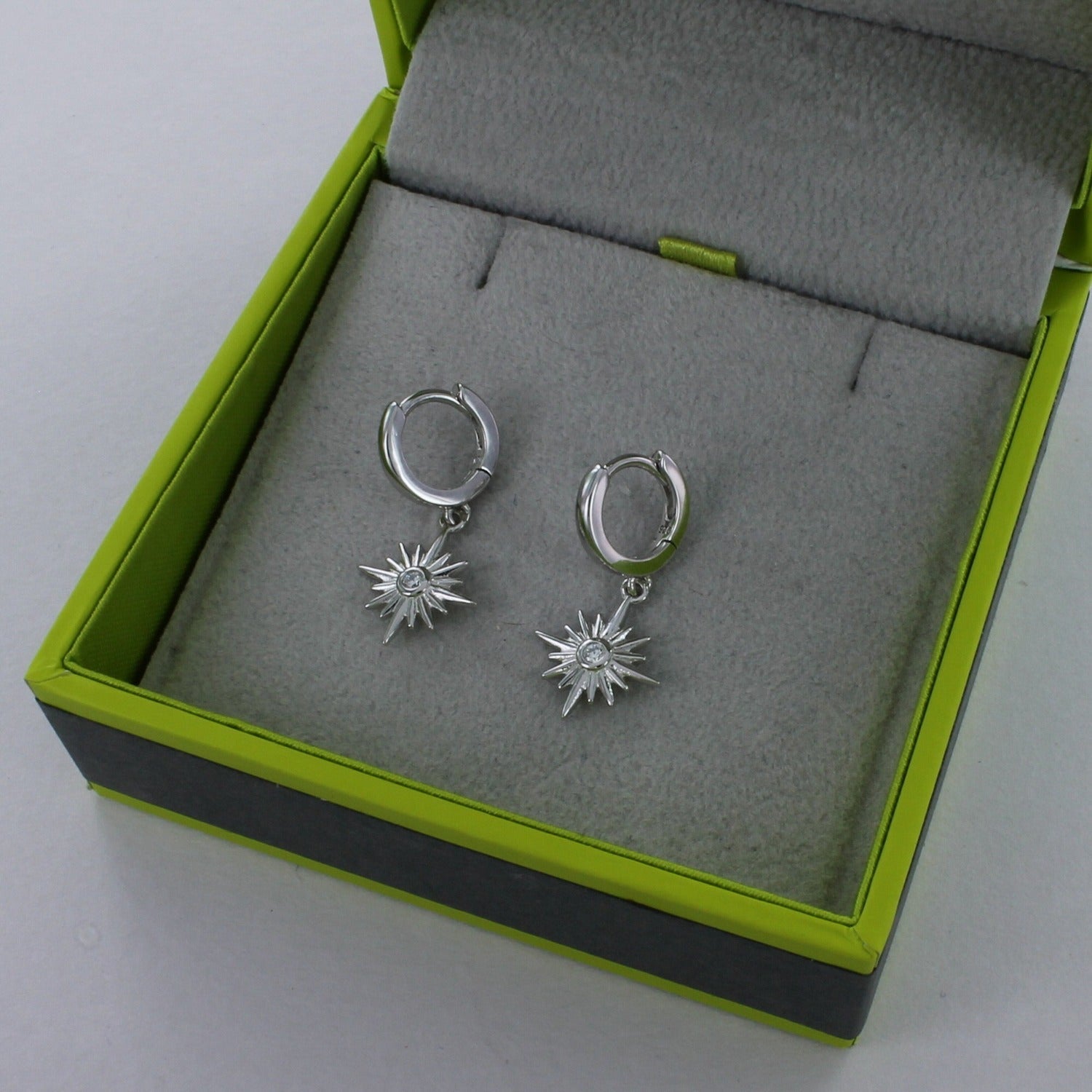 A pair of sterling silver hoop earrings with stars hanging from the bottom and cubic zirconia stones in the centre. The earrings are shown in a Reeves & Reeves gift box.
