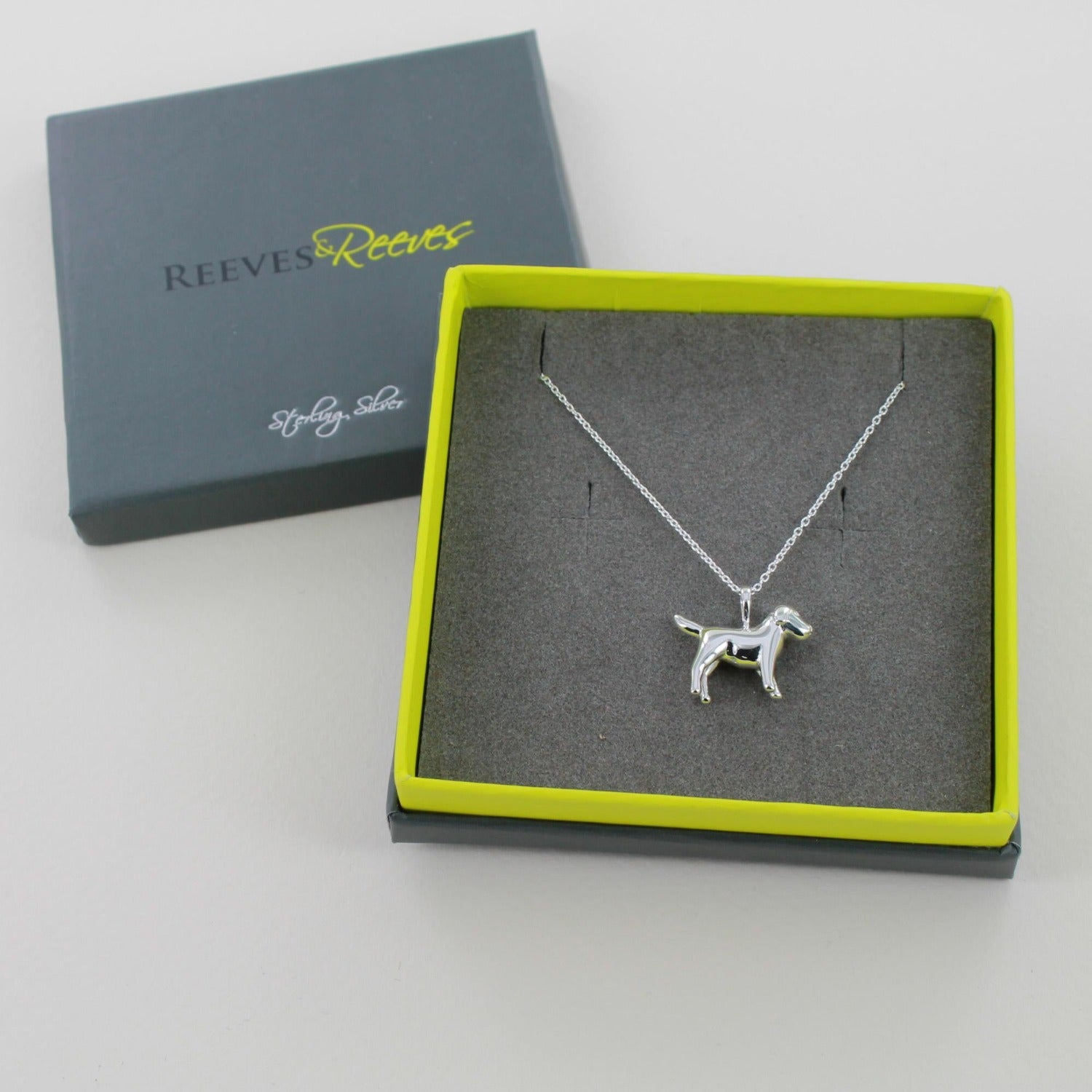 A Sterling Silver Dog Pendant worn on a silver chain and shown in a Reeves & Reeves grey and green branded gift box.