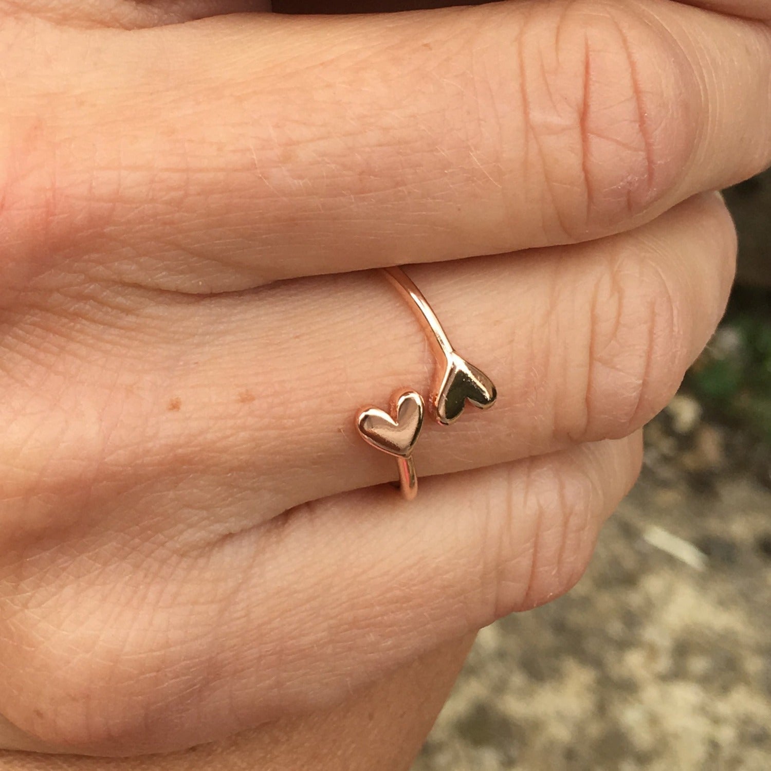 Silver and rose gold plated adjustable ring with heart detail at each end that wraps around the finger. Worn on a hand.
