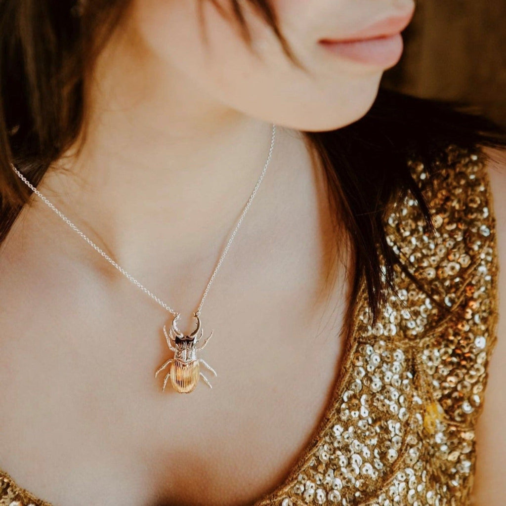 A Sterling Silver Stag Beetle Pendant with gold plated finish on its back and black ruthenium pincers, hung on a silver adjustable chain. Worn on a model.