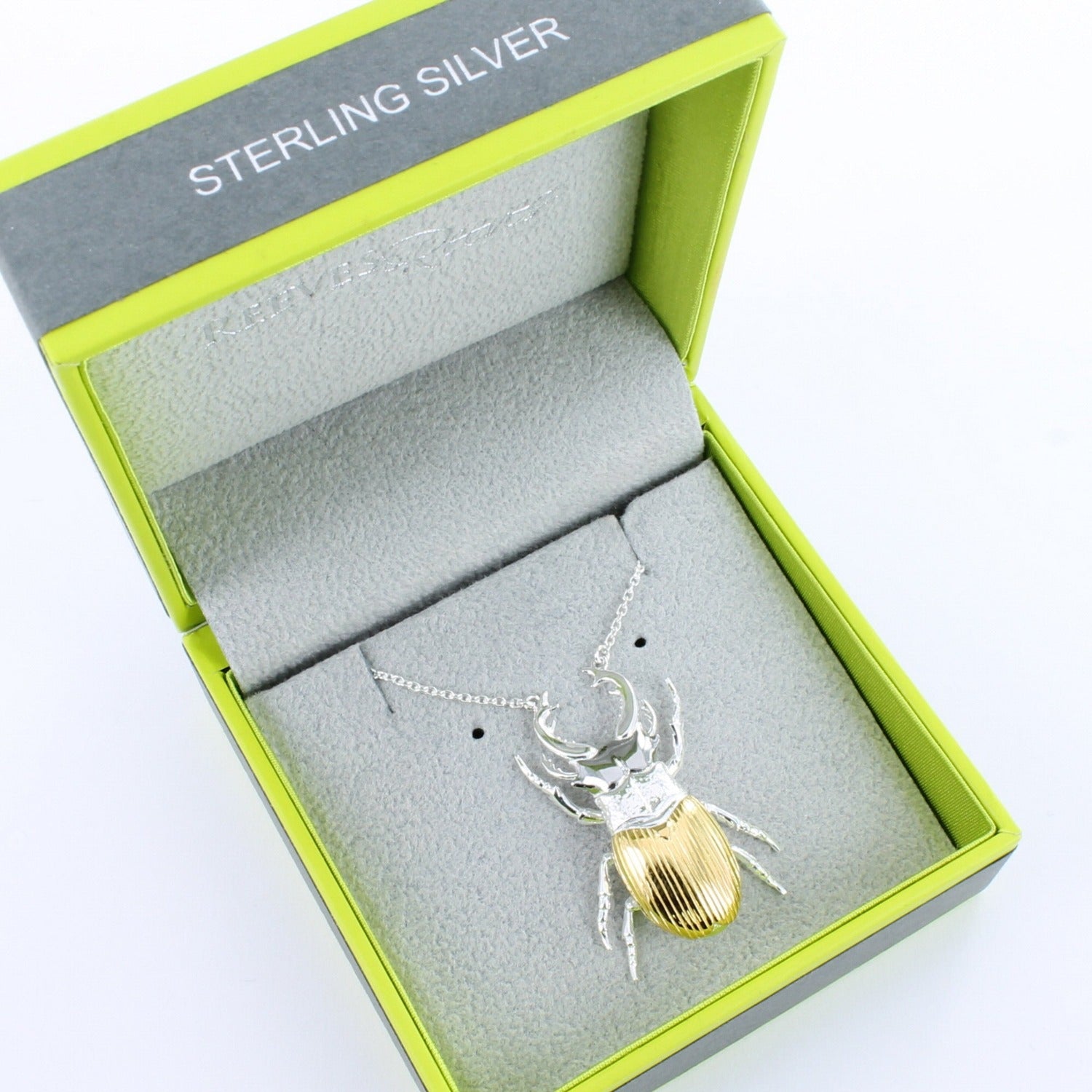 A Sterling Silver Stag Beetle Necklace with a gold plated finish on its back, on a silver chain and shown in a Reeves & Reeves grey and green branded gift box.
