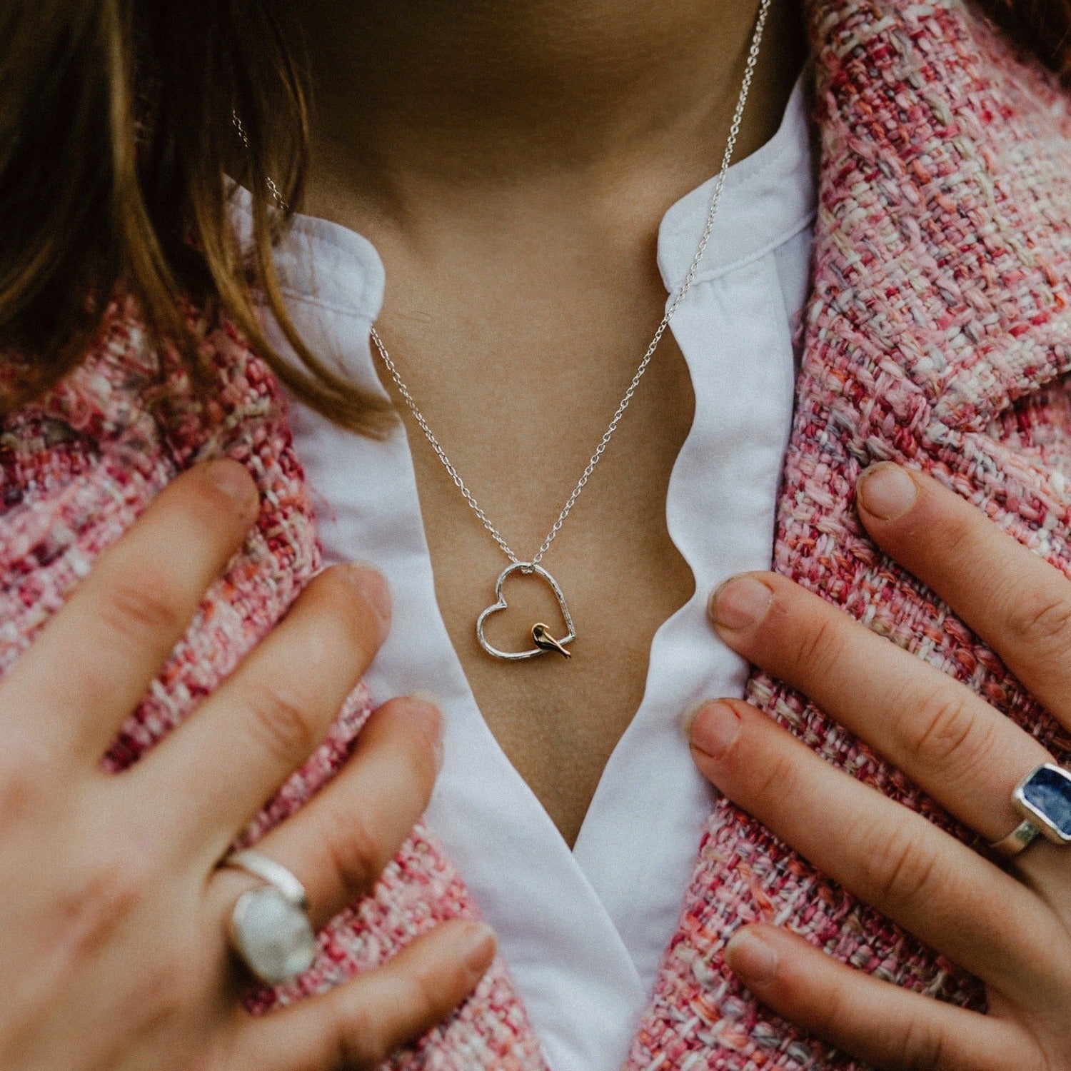 Silhouette heart shaped silver pendant with an 18ct gold plate bird perched inside. The chain is silver and adjustable and is worn on a model wearing an open v neck white blouse.