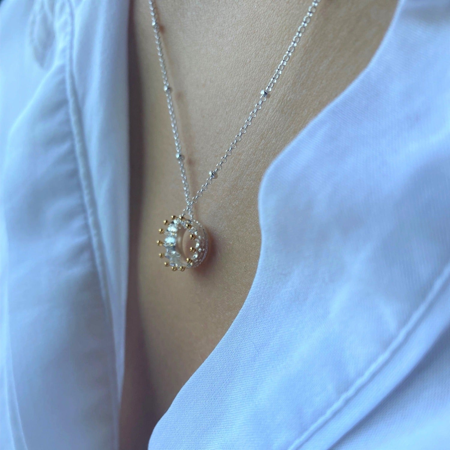 A silver crown necklace with gold plating on its spikes, hung on a silver beaded chain.