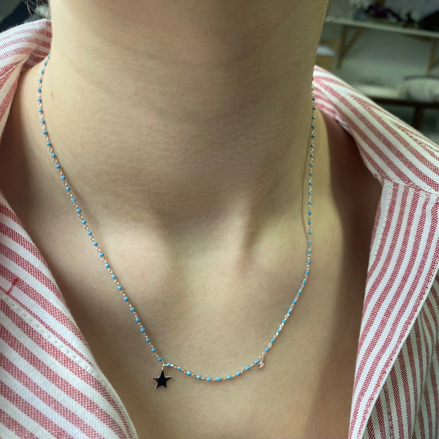 A sterling silver chain necklace with baby blue enamel beads set all the way along the chain. A star charm sits at the central point with a smaller star further up the chain. Worn on a models neck.