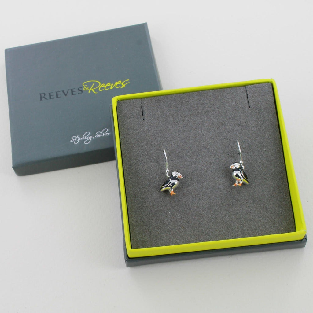 A pair of puffin drop earrings, with black and orange enamel detail, shown in a Reeves & Reeves gift box.