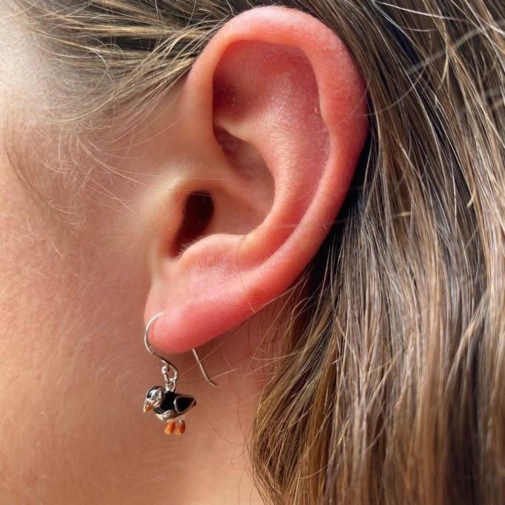 A sterling silver Puffin Drop Earring, with black and orange enamel detail and shown in a ladies ear.