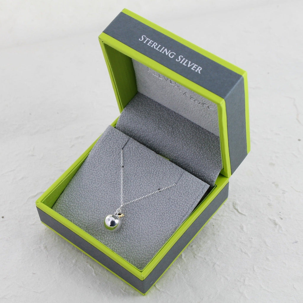 A silver apple pendant with gold leaf detail, hung on a silver chain and shown in a Reeves & Reeves grey and green branded gift box.