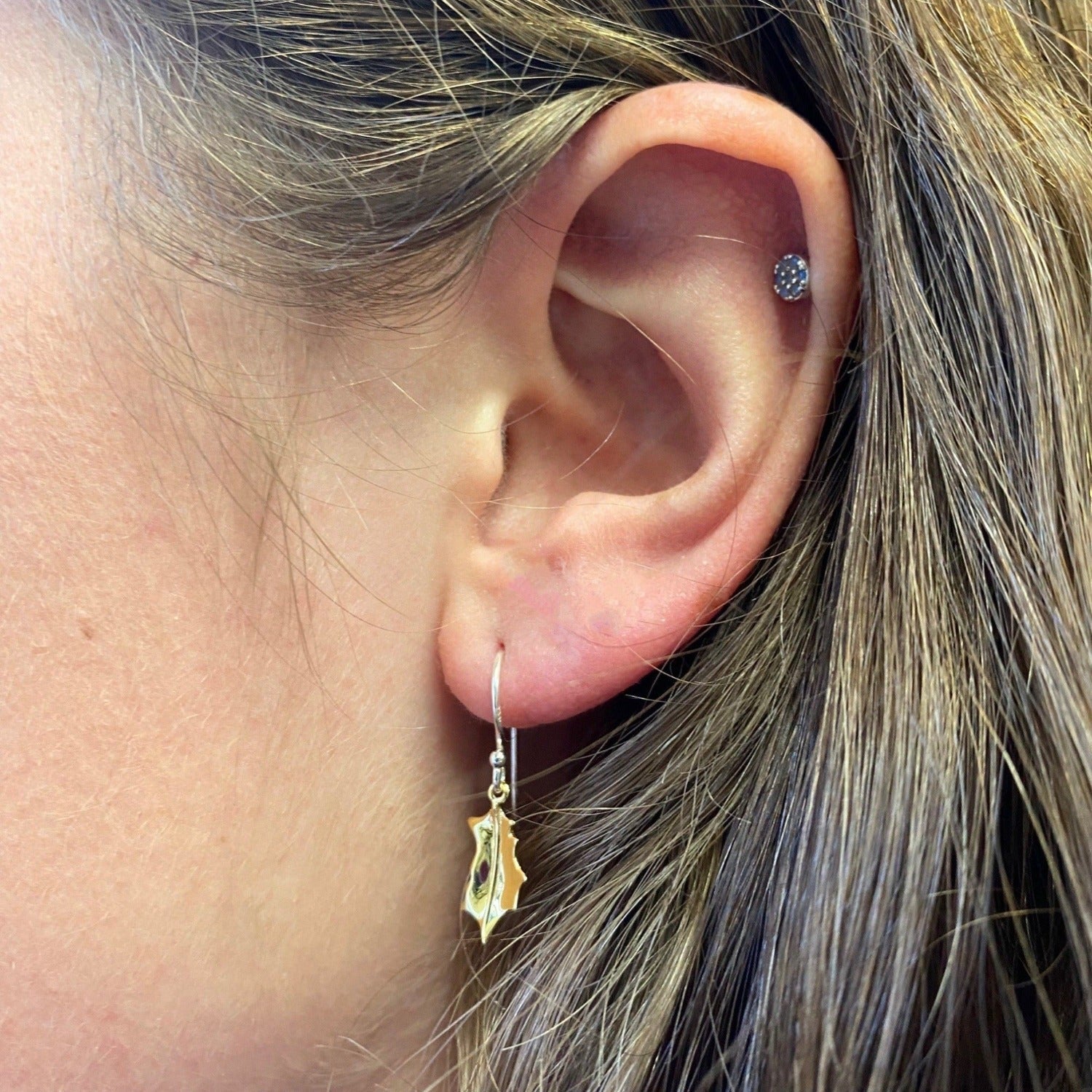 A Holly drop earring in sterling silver with 18ct gold plating and hanging on silver hooks. Shown in a ladies ear.