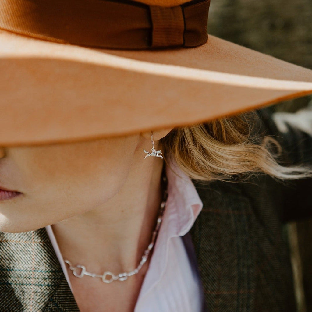 A sterling silver racing horse earring, hanging on a silver hook and shown in a ladies ear.