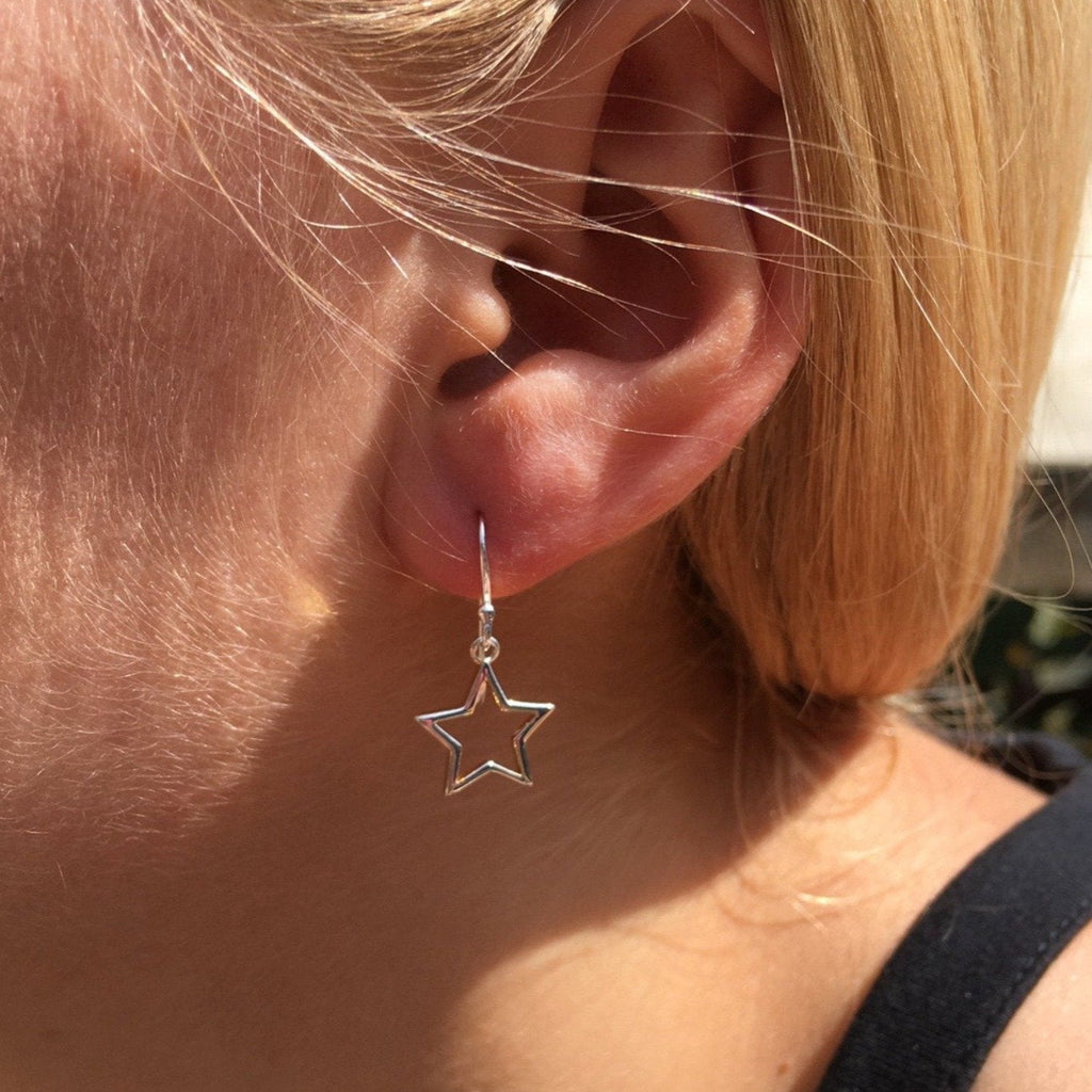 Star drop earrings in silver being worn by a model. 