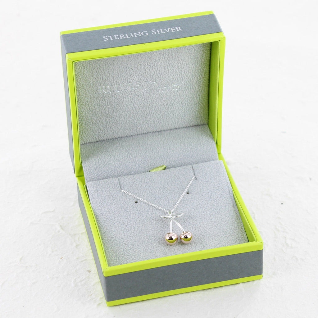 A silver and rose gold plated cherry necklace on a silver chain and shown in a Reeves & Reeves branded gift box.