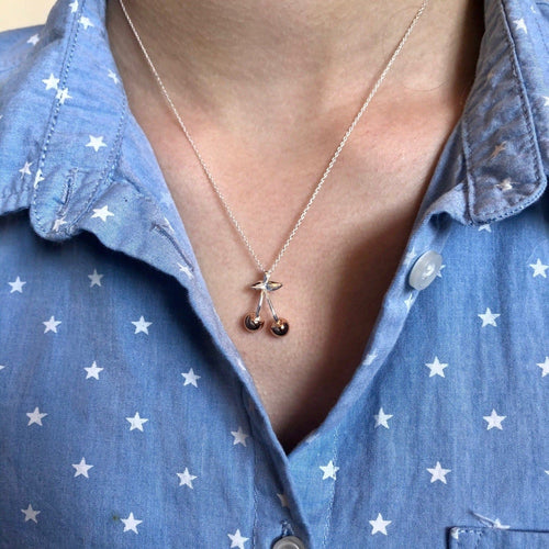 A silver and rose gold plated cherry necklace, hung on a silver chain and worn on a models neck.