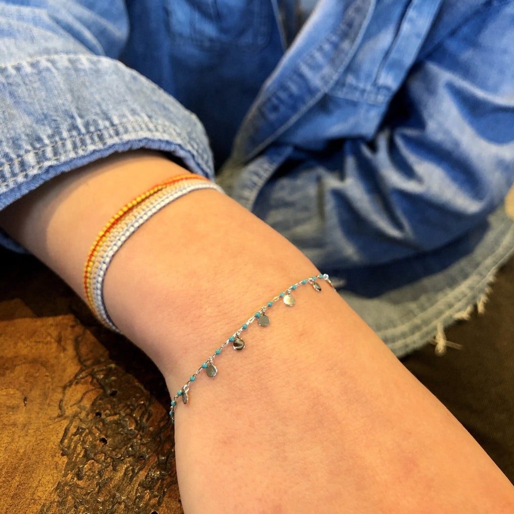 Silver and turquoise bead bracelet with high shine silver disc charms hanging from the chain. Worn on a ladies wrist.