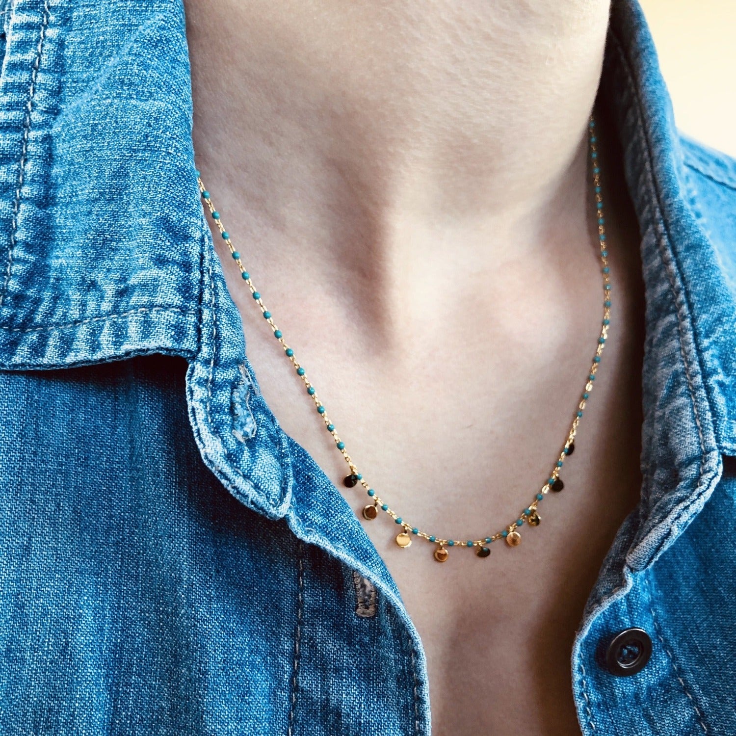 Turquoise and gold plate enamel beaded necklace with high shine discs sat centrally along the chain, worn on a models neck