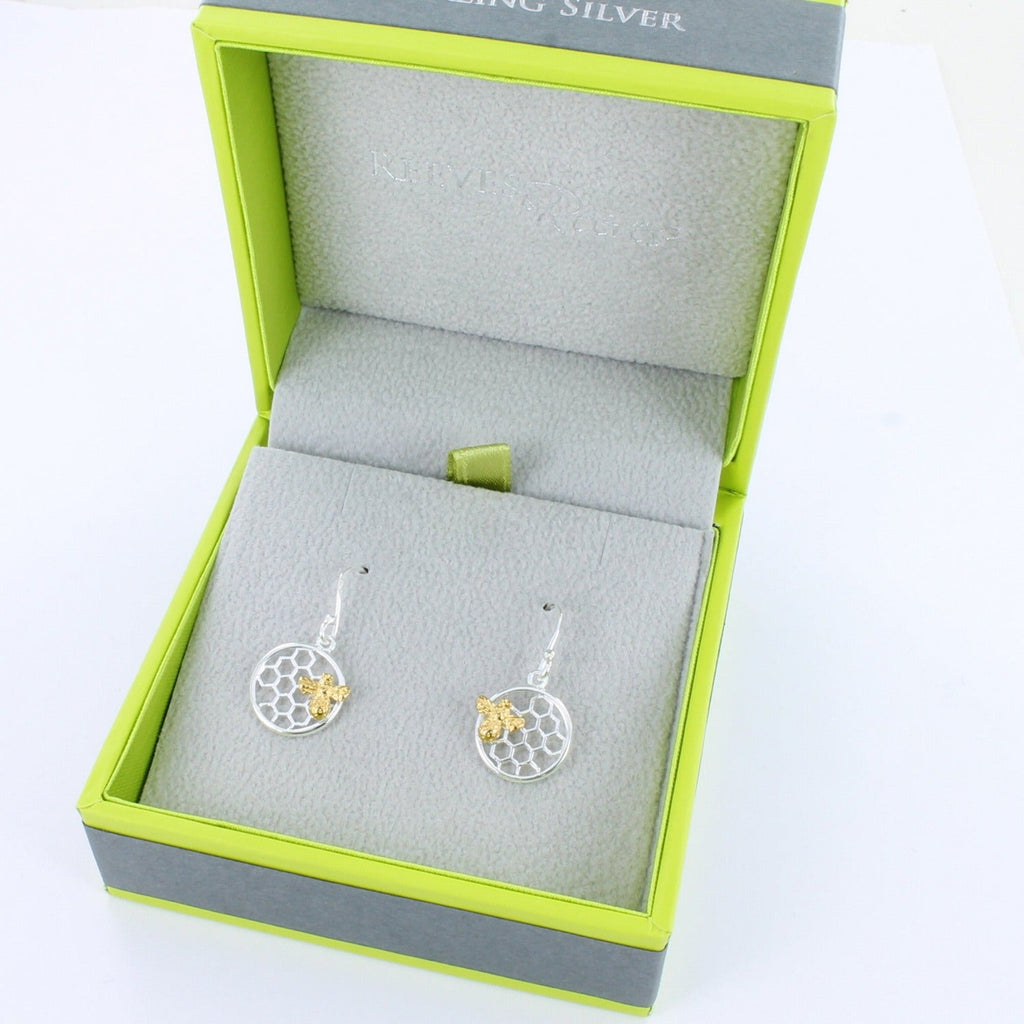 A pair of sterling silver circular shaped earrings with a honeycomb design in the centre, and an 18ct gold plated bee sat on the front. Hanging on silver hooks and shown in a Reeves & Reeves gift box.
