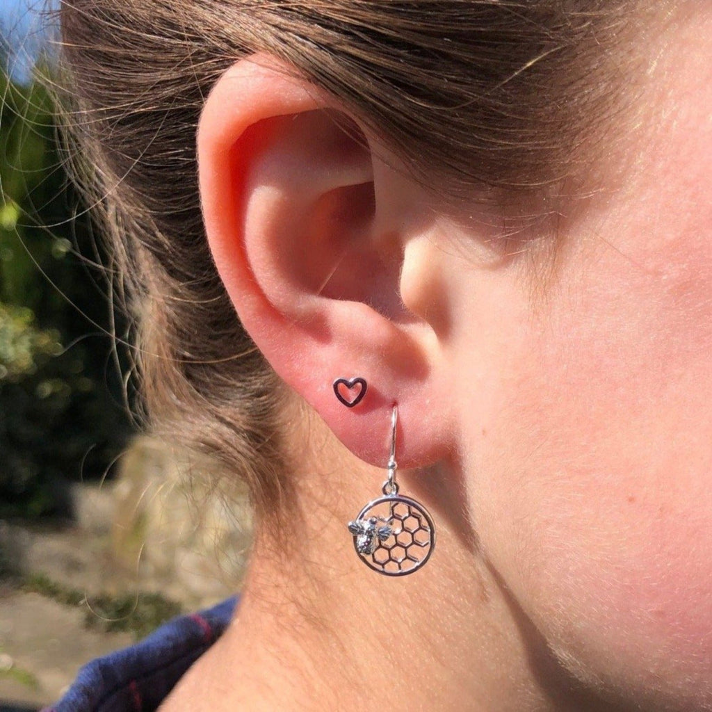A circular earring with a honeycomb design in the centre, and a silver detailed bee stuck to the front of the honeycomb. Hanging on a silver hook and shown in a ladies ear.