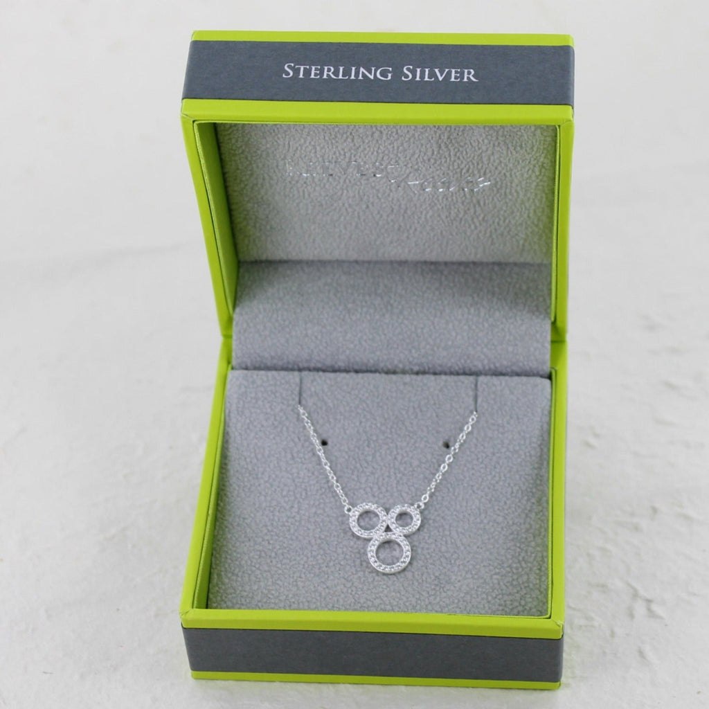 A sterling silver necklace featuring three circular shapes set with cubic zirconia stones and hung on a silver chain. Shown in a Reeves & Reeves branded gift box.