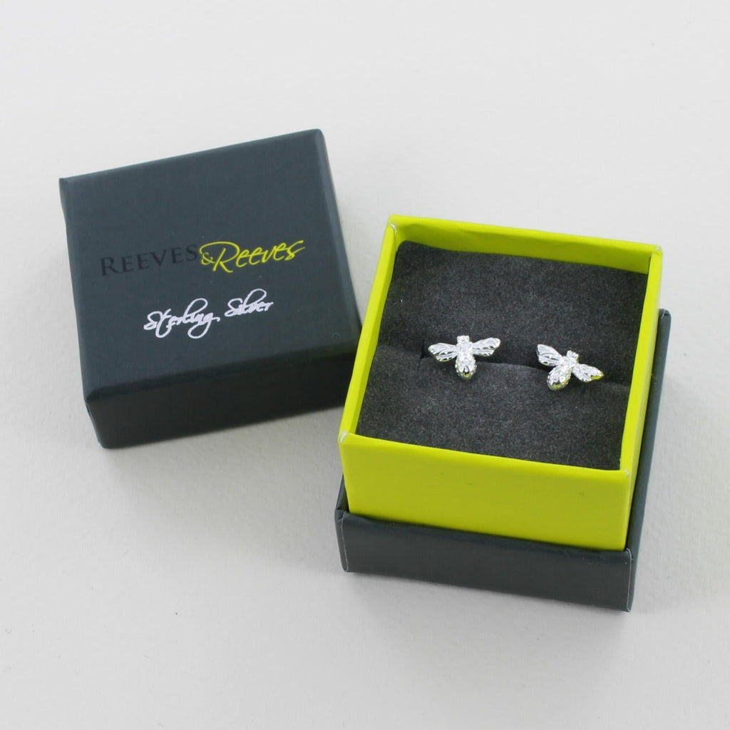 A pair of sterling silver bumble bee stud earrings, shown in a Reeves & Reeves grey and green gift box.