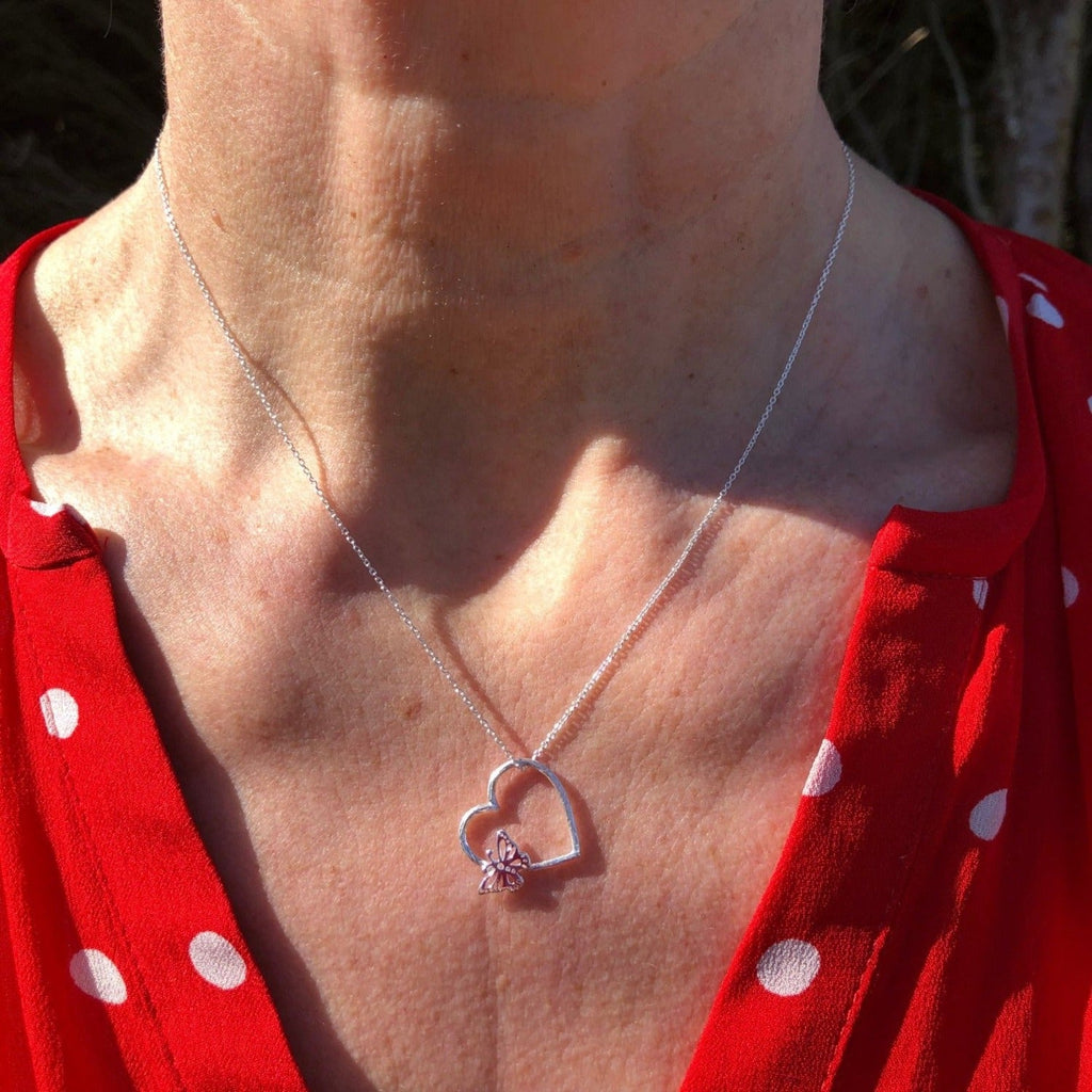 A Sterling Silver heart silhouette pendant with a butterfly sat on the edge, hung on a silver adjustable chain and worn on a model.