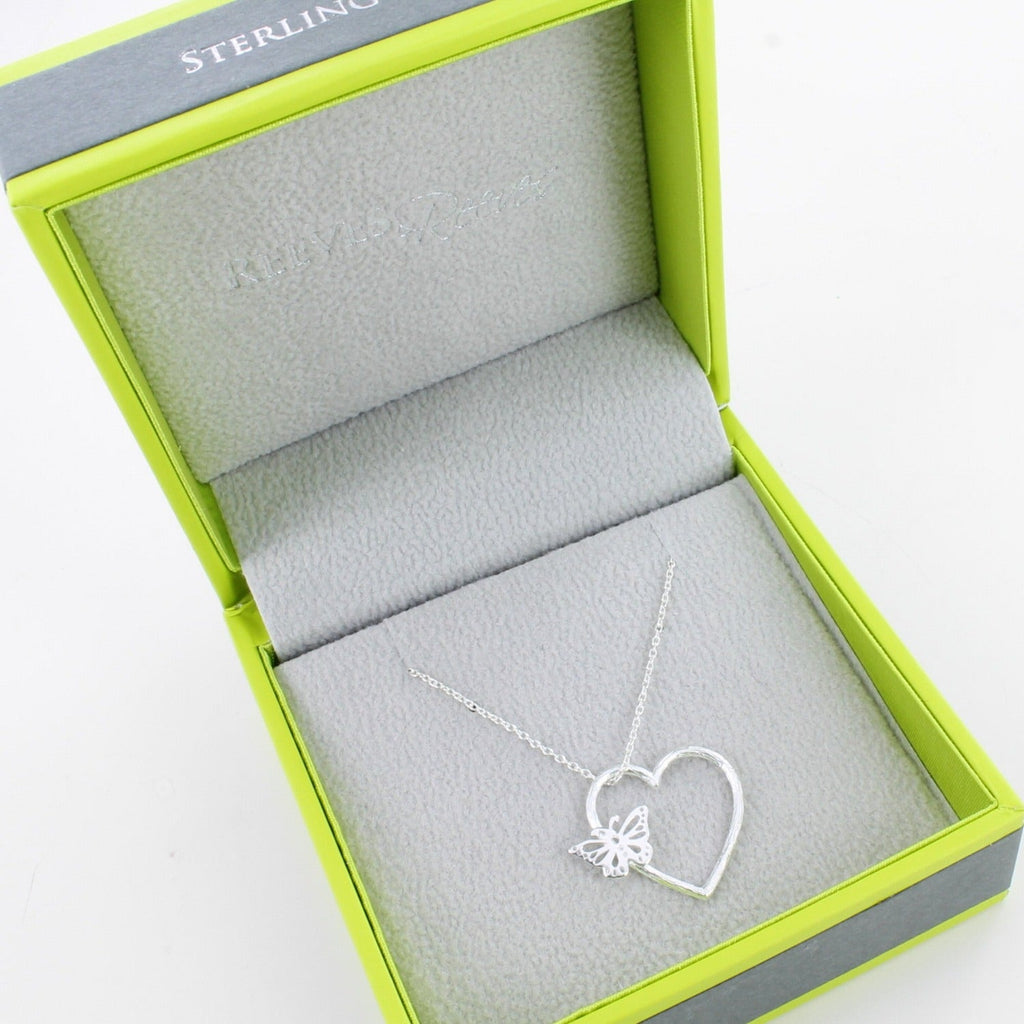 A Sterling Silver heart silhouette pendant with a butterfly sat on the edge, hung on a silver chain and shown in a Reeves & Reeves grey and green branded gift box.