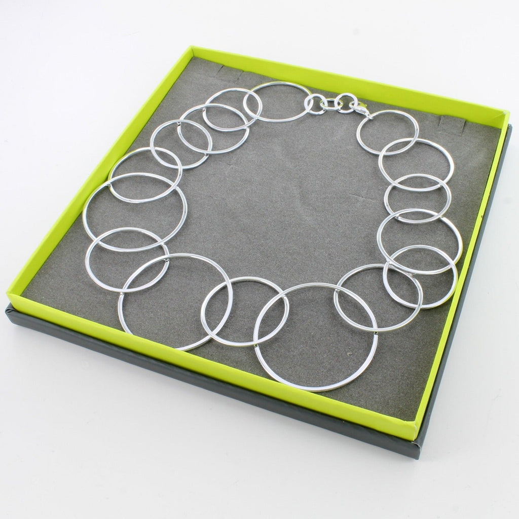 A sterling silver necklace made up of interlinking circles of varying sizes, shown in a Reeves & Reeves grey and green branded gift box.