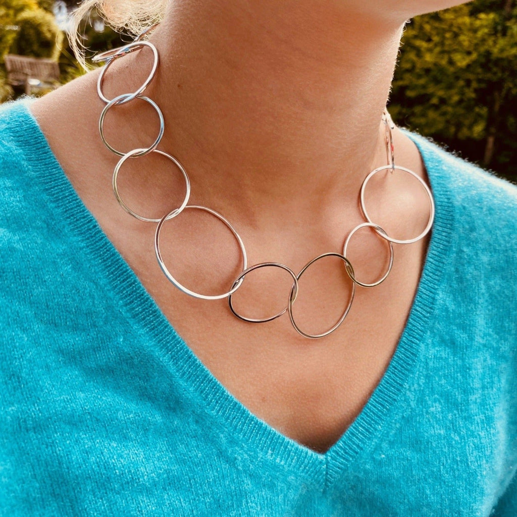 A sterling silver necklace made up of interlinking circles of varying sizes that continue around the neck. Worn on a model.