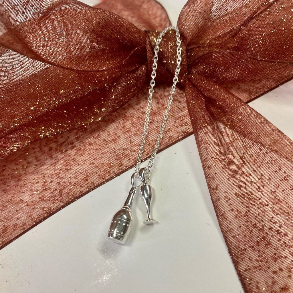 A Sterling silver champagne bottle charm, hanging next to a glass and on a silver adjustable chain.