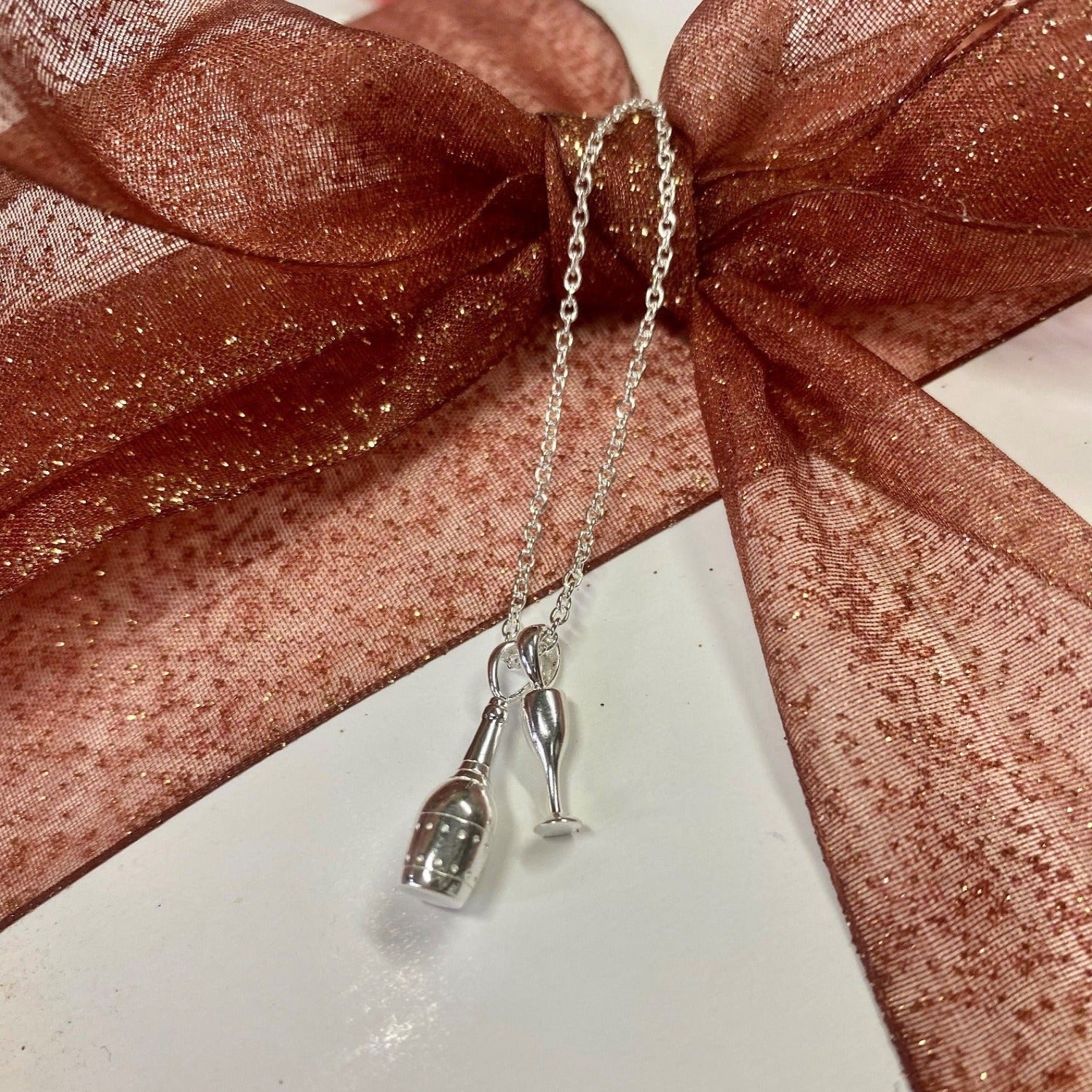 A Sterling silver champagne bottle charm, hanging next to a glass and on a silver adjustable chain.
