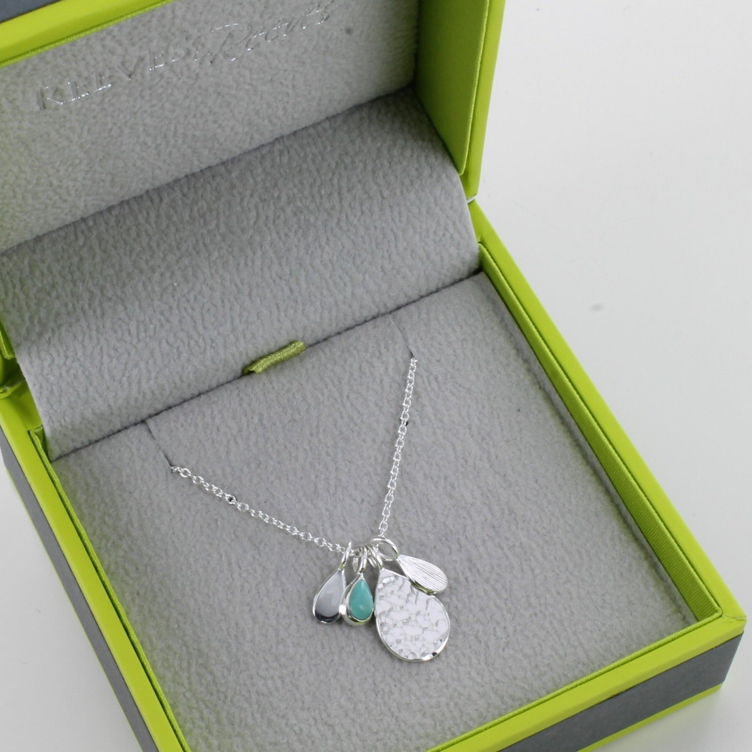 Sterling Silver Pear drop hammered charm with three smaller charms in silver and one with a turquoise stone, all hanging from a silver chain and shown in a Reeves & Reeves box.