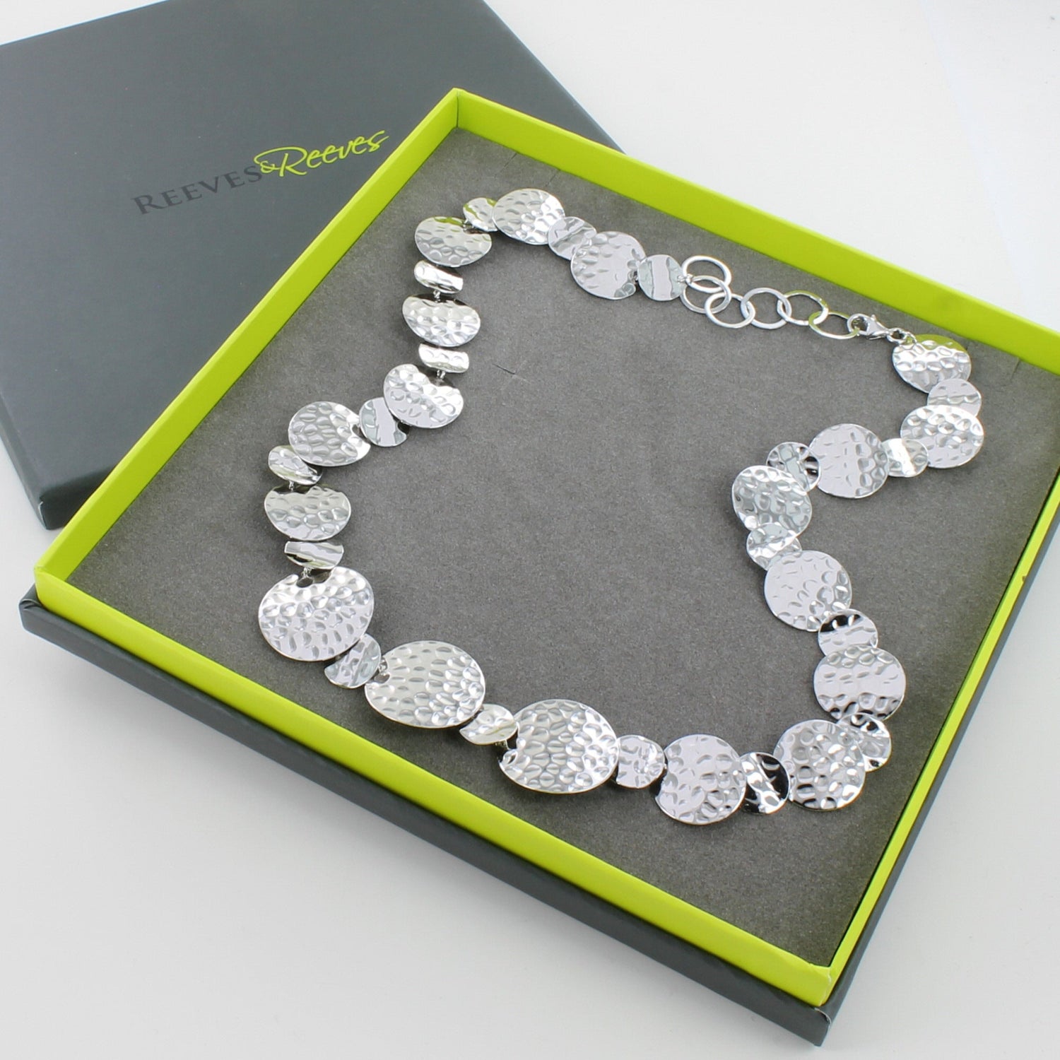 A sterling silver necklace with circular discs that have a hammered finish, adjoined by a slight overlap and in a continuous design. Shown in a Reeves & Reeves gift box.