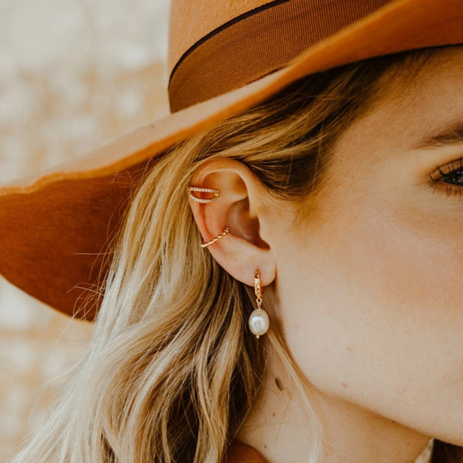 A lady wearing a pearl earrings and two ear cuffs.