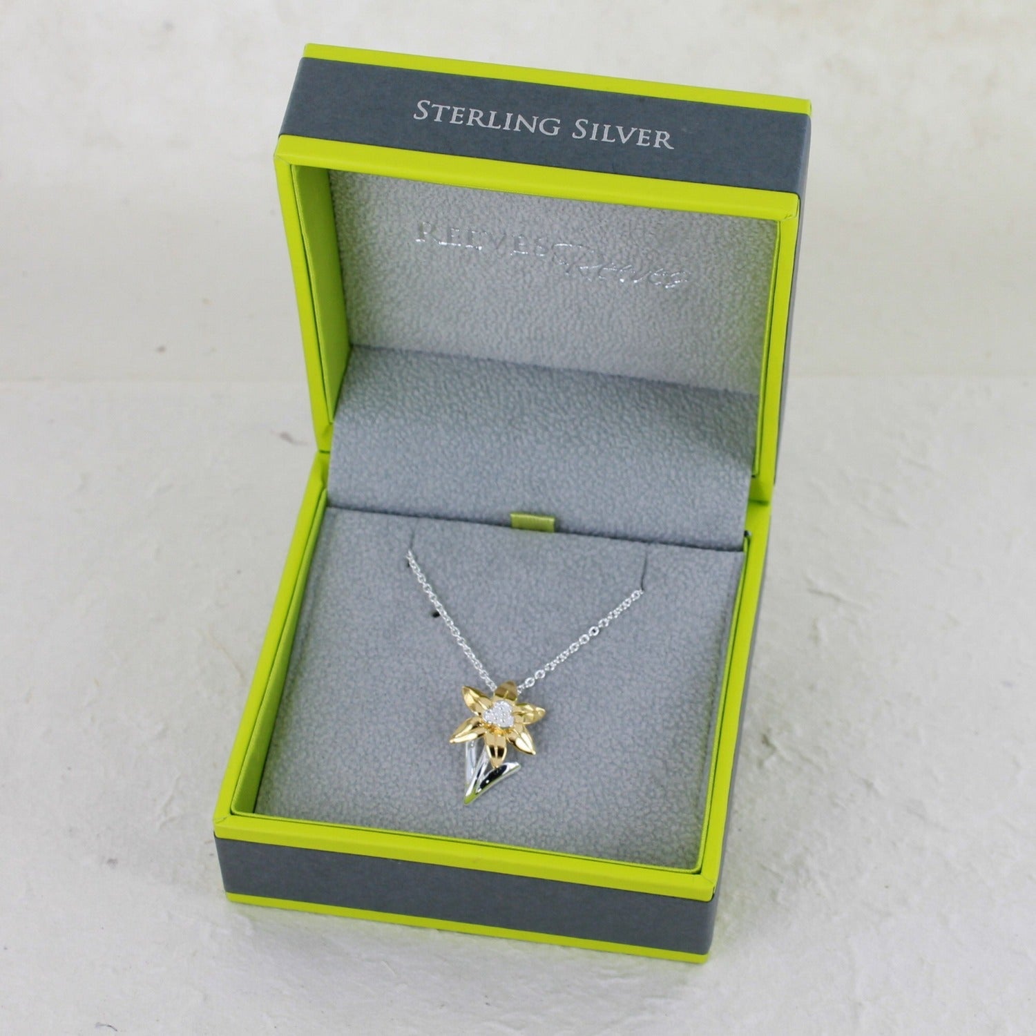 Sterling Silver Daffodil Necklace with gold plated leaves, hung on a silver chain and shown in a Reeves & Reeves gift box.