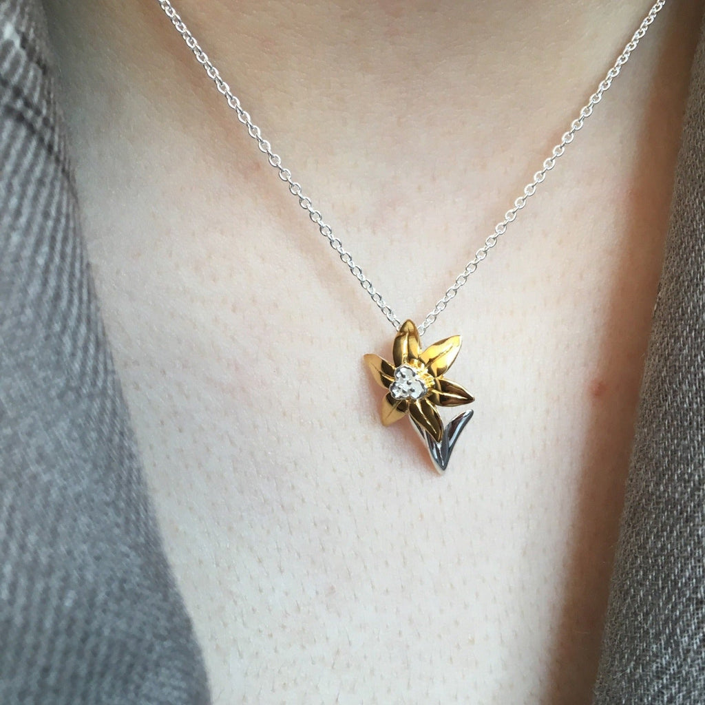 A Sterling Silver Daffodil Necklace with gold plated leaves, hung on a silver chain and worn on a models neck.