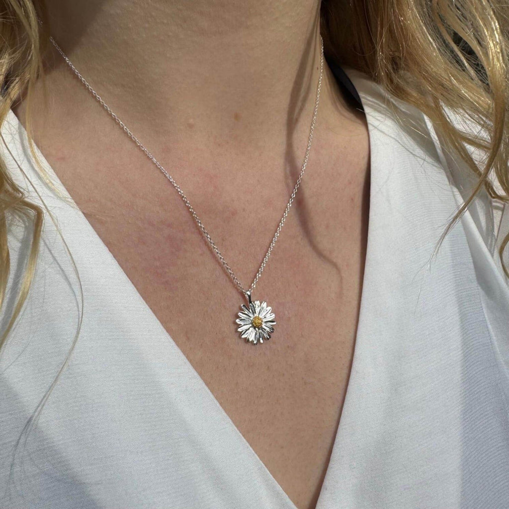 A silver daisy pendant with a gold plated centre, hanging on a silver adjustable chain and worn on a model.