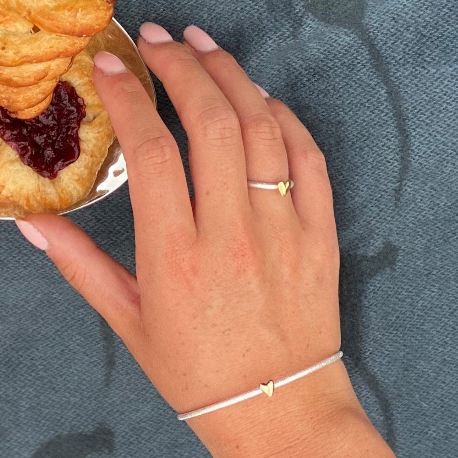 A fine silver matt finish bangle, with a gold plated heart on the front, worn on a wrist with the matching ring.
