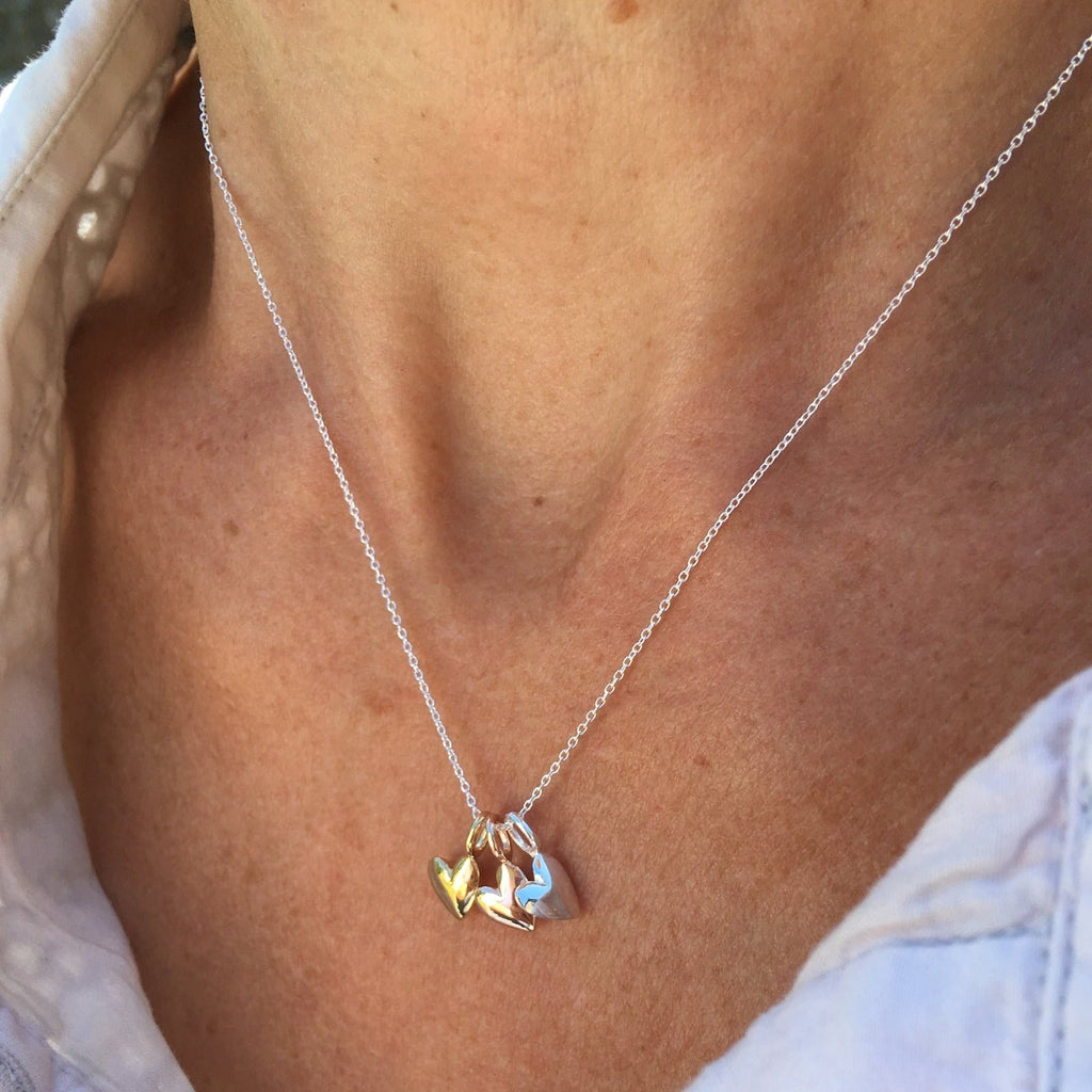 Trio of heart charms on a silver chain in sterling silver, 18ct yellow or rose gold, hanging on a silver chain on a models neck.