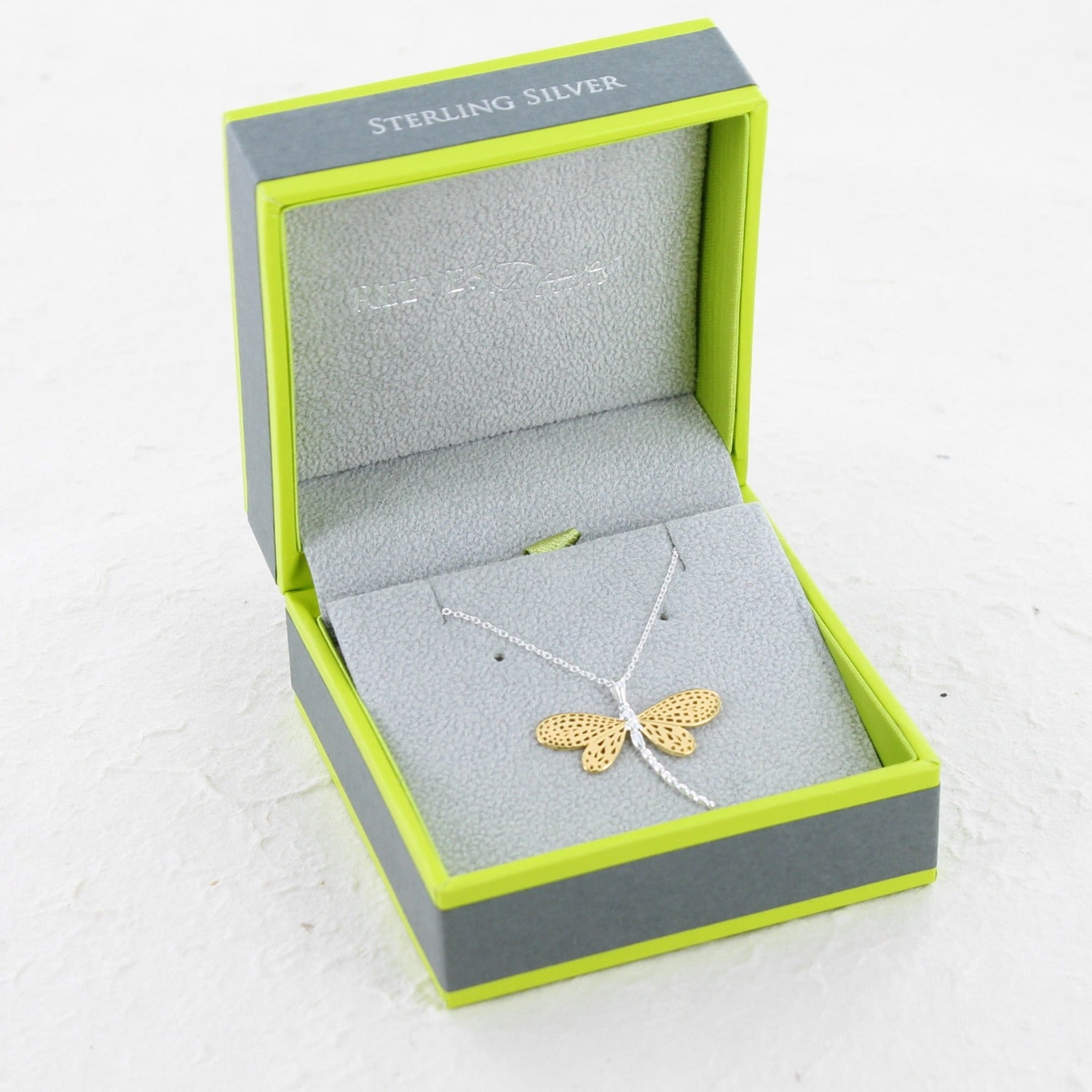 gold and silver dragonfly pendant on a chain being shown in a Reeves & Reeves branded gift box, in the brand colours green and grey.