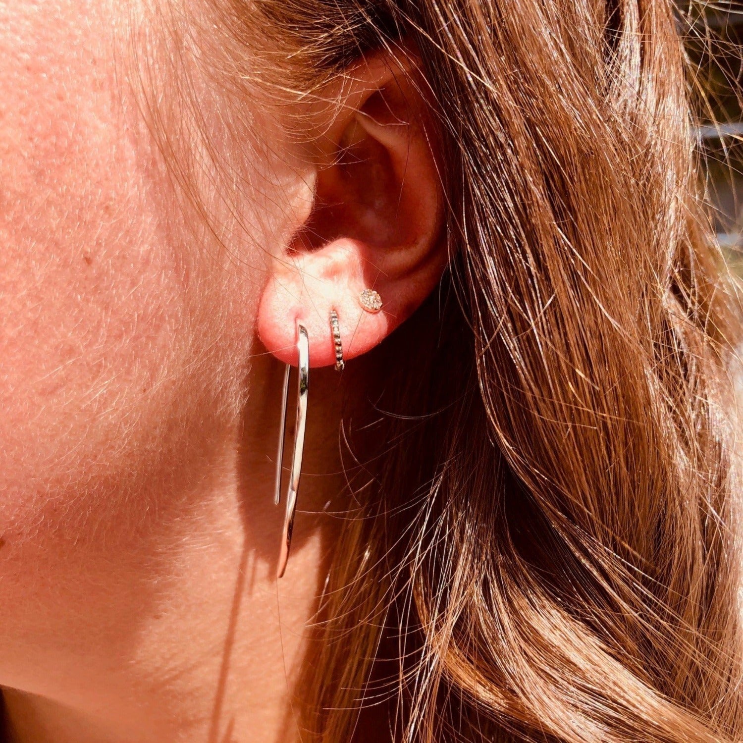 A sterling silver elegant earring which curves through the ear. Shown on a ladies ear with other piercings.