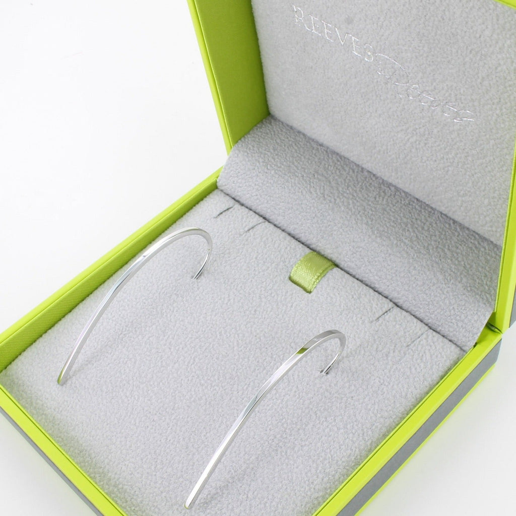 A pair of sterling silver elegant earrings in a curve shape and shown in a Reeves & Reeves gift box.