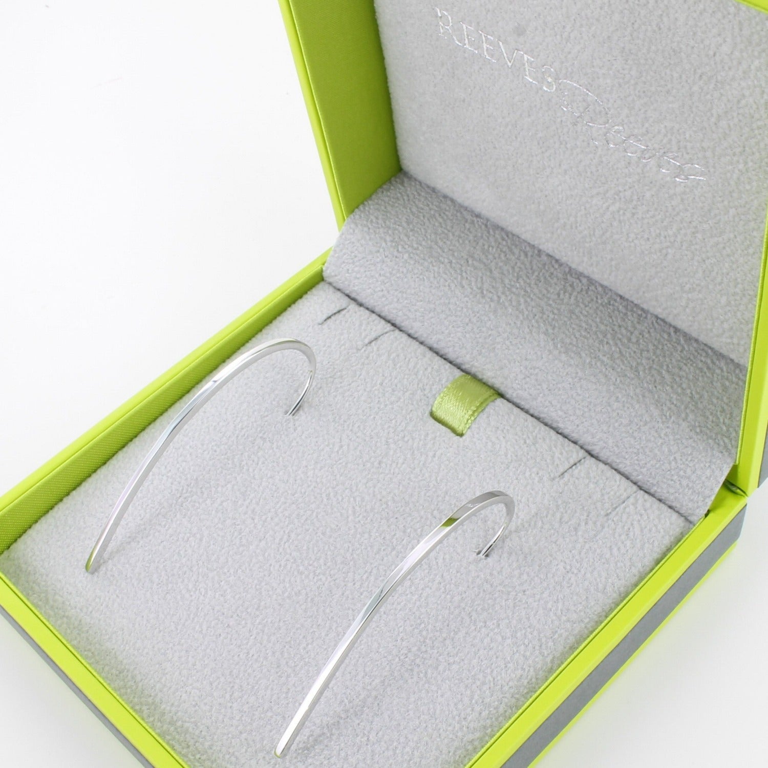 A pair of sterling silver elegant earrings in a curve shape and shown in a Reeves & Reeves gift box.