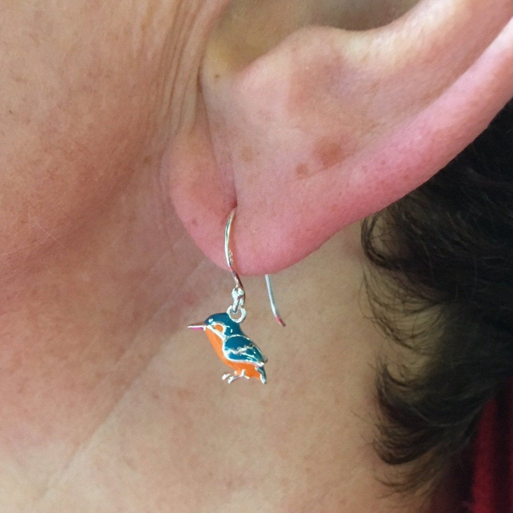 A Kingfisher drop earring, in silver and blue and orange enamel detail, shown in a ladies ear.