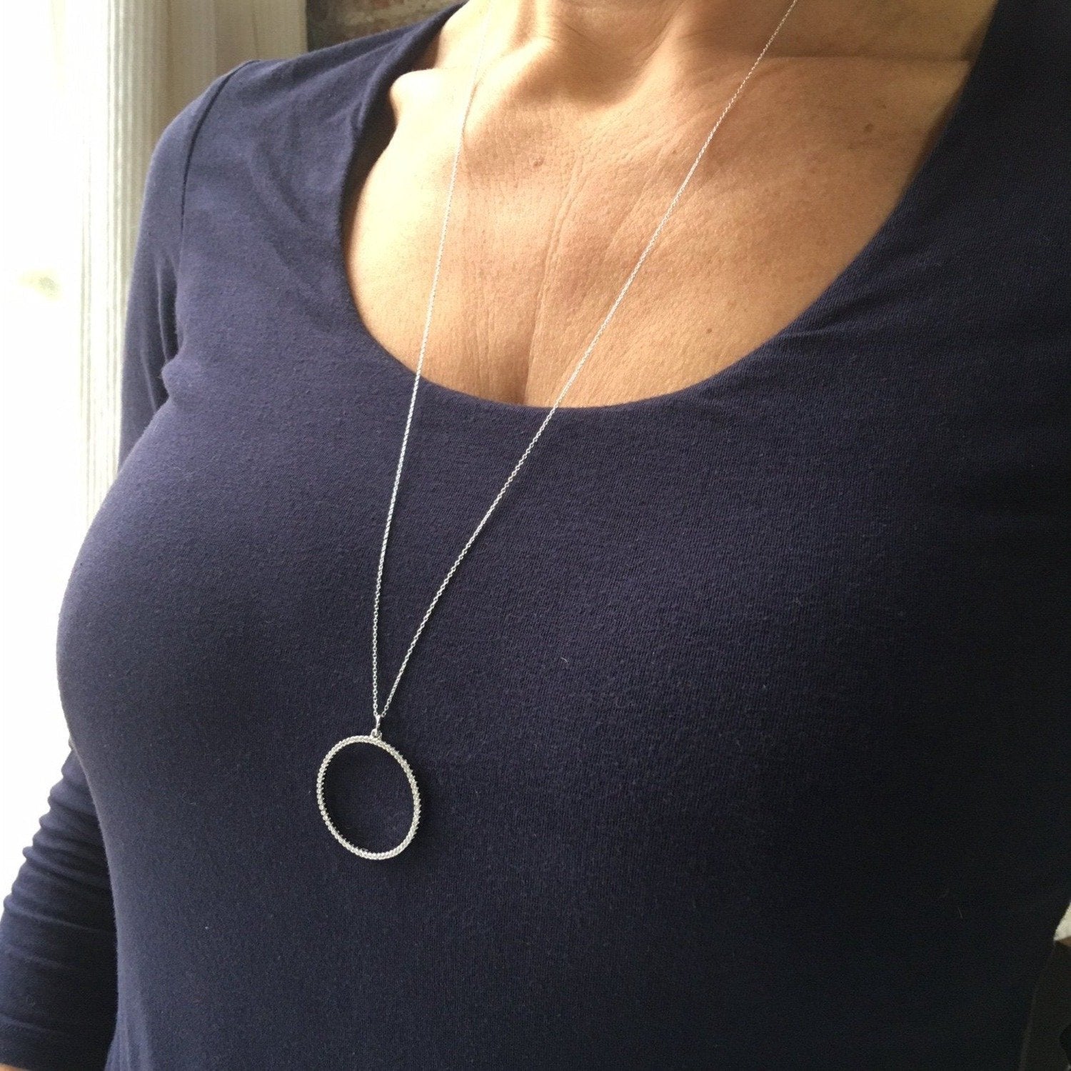 A sterling silver circular outline pendant filled with cubic zirconia stones. Hung on a long silver chain and worn on a ladies neck over a t shirt.