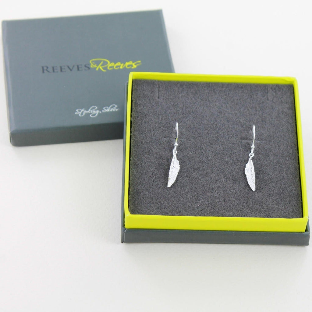 A pair of sterling silver feather drop earrings, hung on silver hooks and shown in a Reeves & Reeves grey and green gift box.