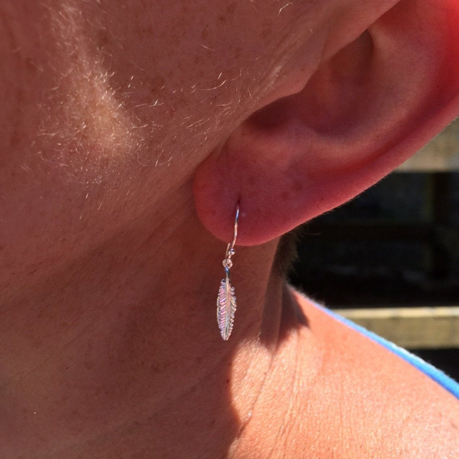 A sterling silver feather drop earring, worn in a ladies ear.