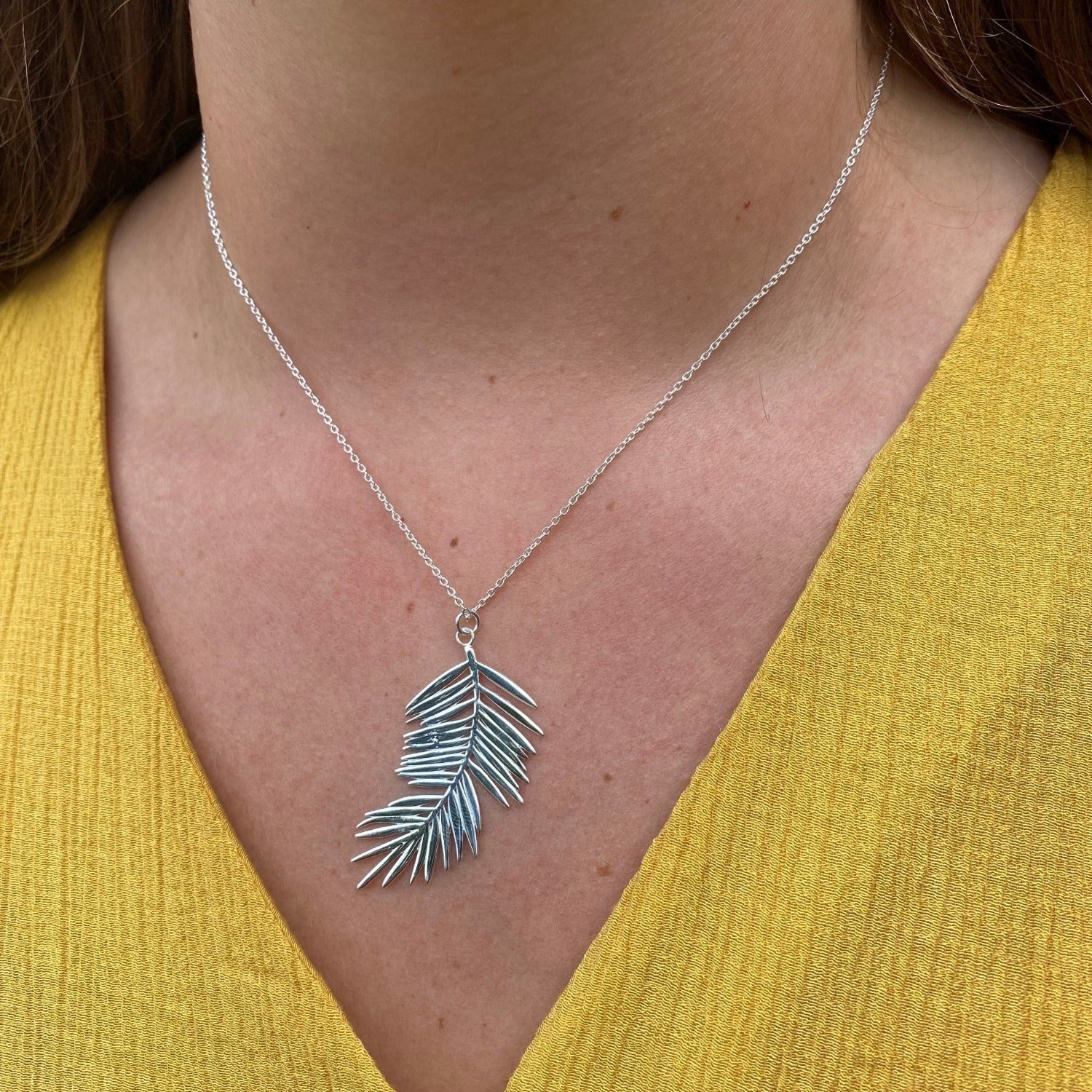 Sterling Silver Fern Leaf Pendant, hanging on a silver chain and worn on a models neck.