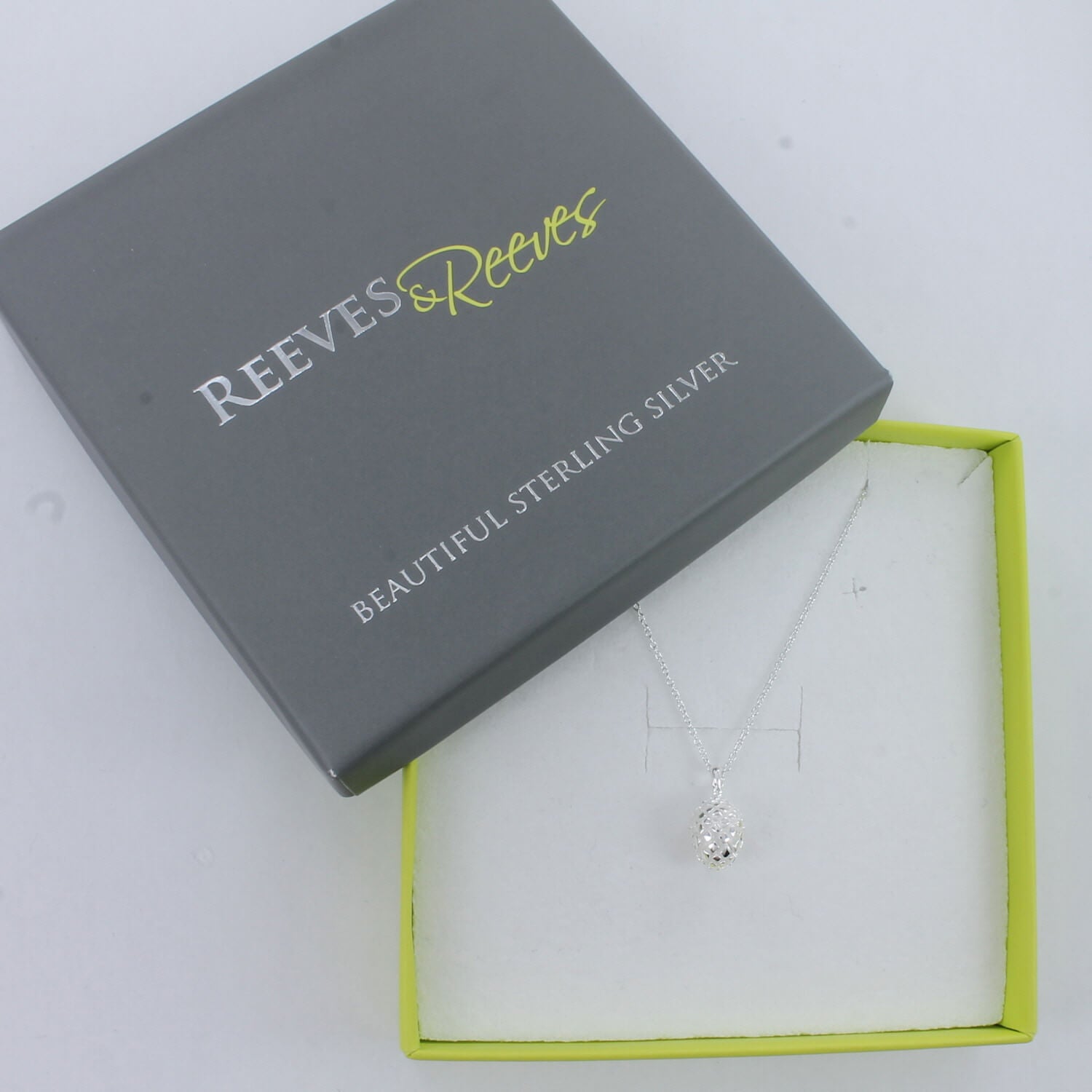 A silver Fir cone Necklace, hung on a silver chain and shown in a Reeves & Reeves grey and green gift box.