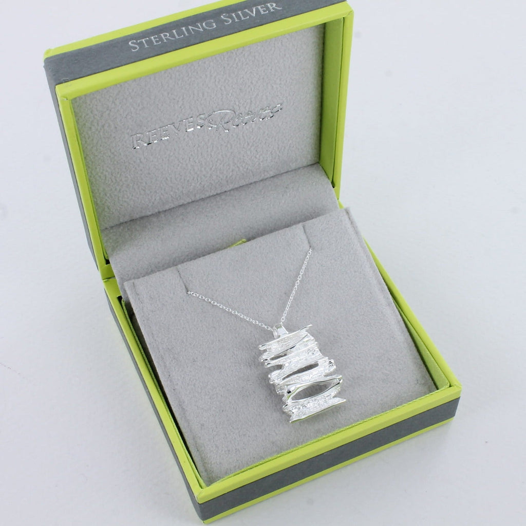 A sterling silver flaky pendant, hung on a silver chain and shown in a Reeves & Reeves grey and green branded gift box.