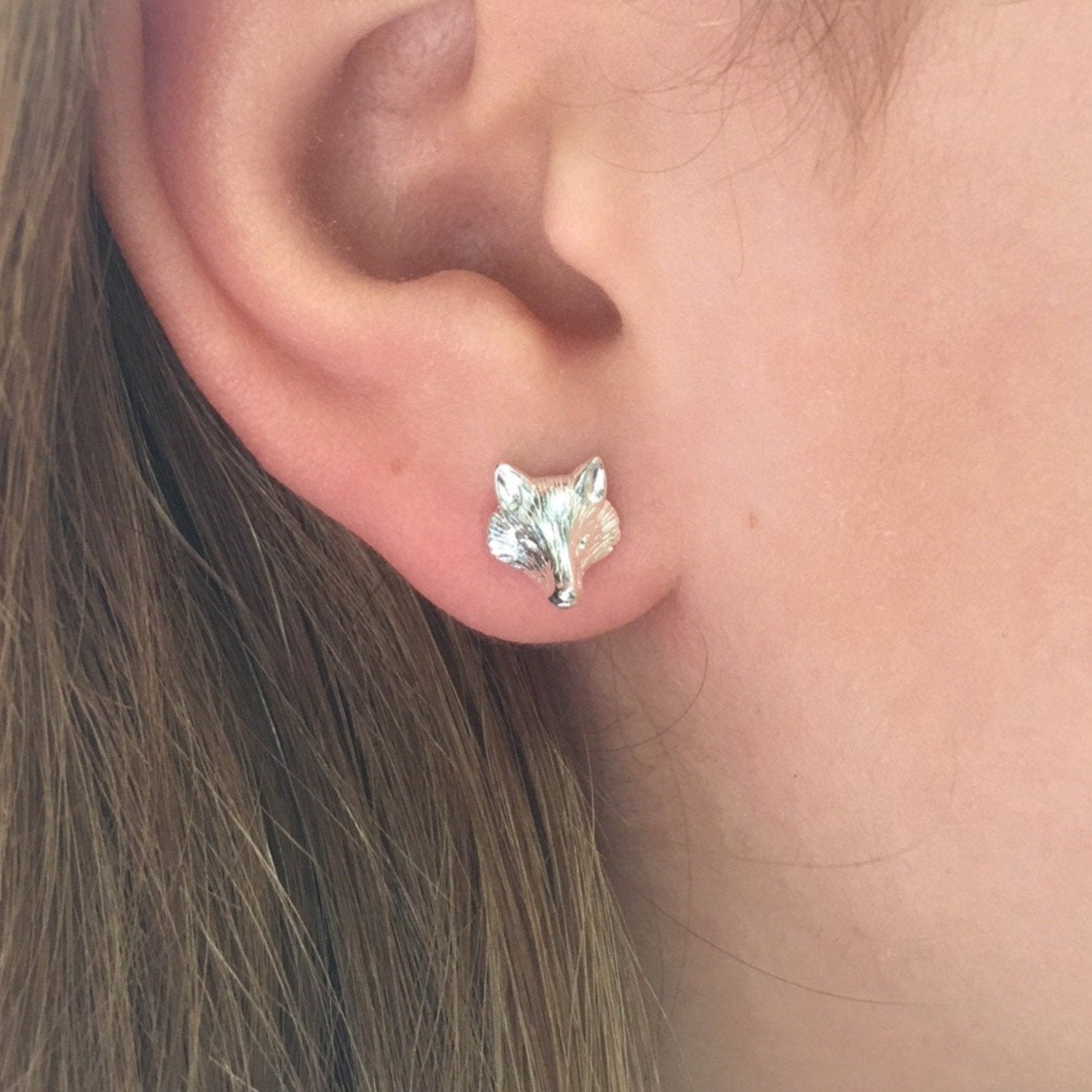 A sterling silver Fox head Stud Earring, shown in a ladies ear.