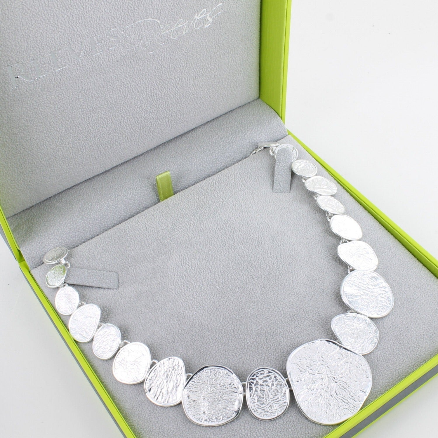 A sterling silver necklace with varying irregular circular shapes that have textured finish, shown in a Reeves & Reeves gift box.