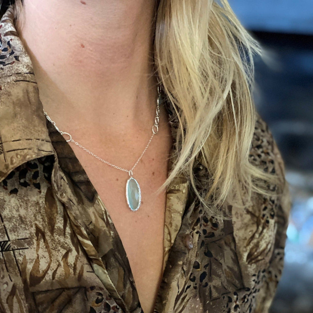 A sterling silver chain necklace with an oval aqua chalcedony as the central feature, worn on a model.